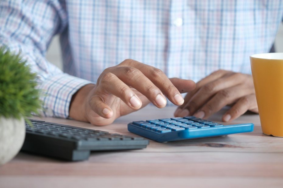 person using calculator at desk with coffee mug